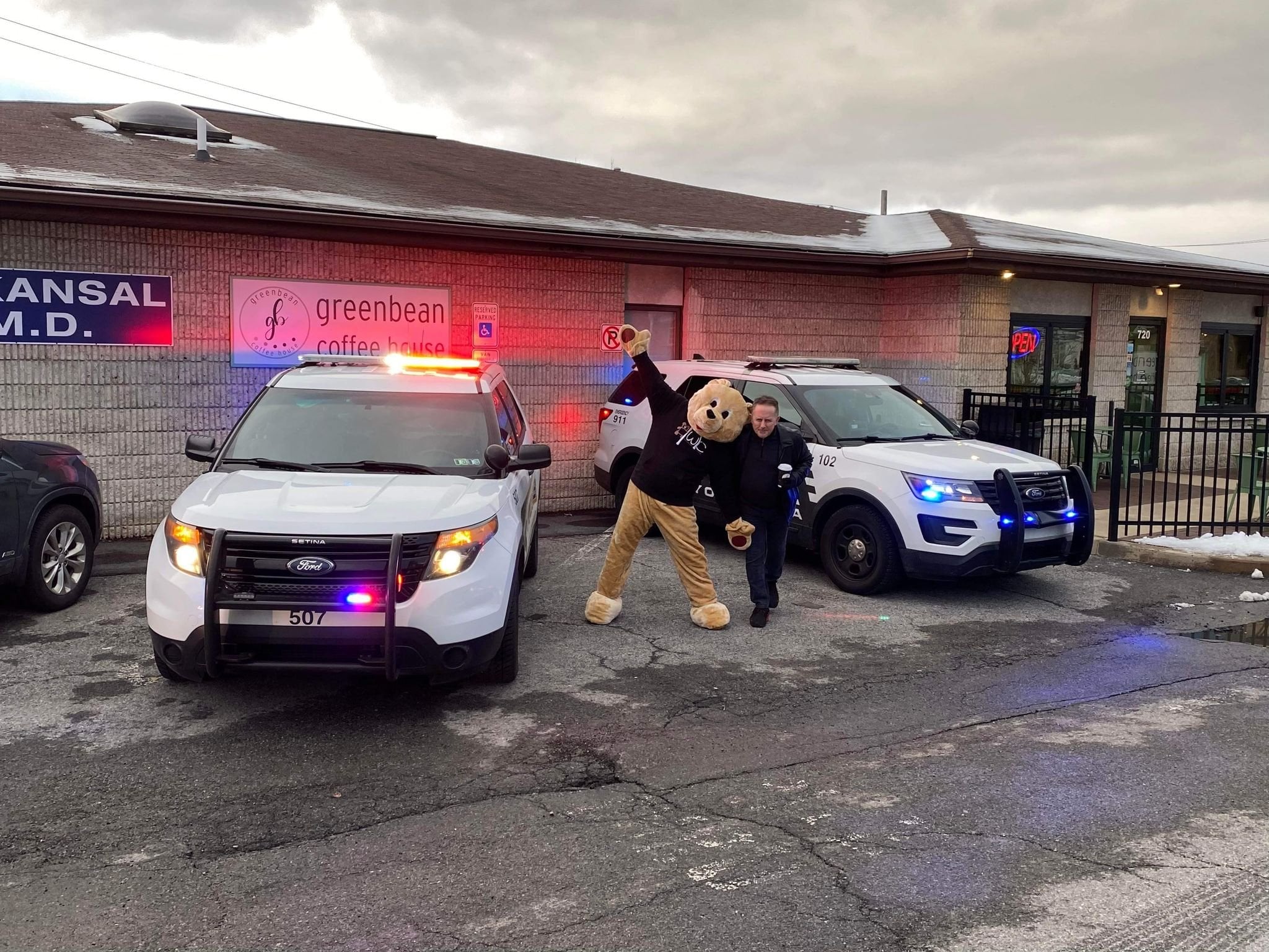 BWC mascott and person posing between two police cars with flashing lights.