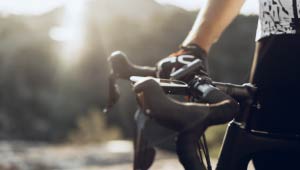 A picture of bicycle handles and a person's hand holding them.