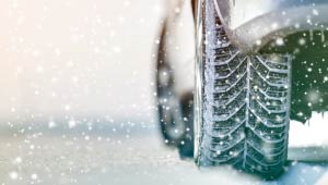 A picture of a lower portion of a car navigating through a snow covered road during a snow storm.